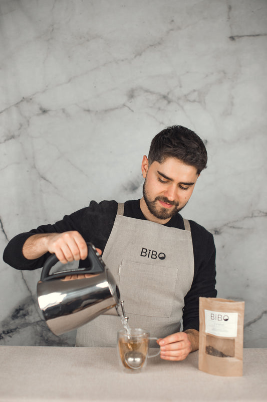 Benjamin versant de l'eau chaude dans une tasse avec une boule à thé rempli du mélange L'Original